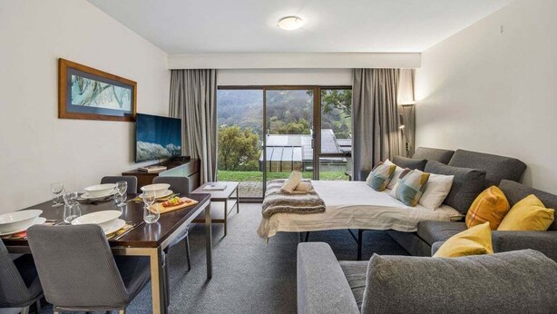A hotel room with a bed, sofa, dining table, and TV.