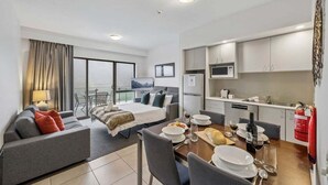 Una habitación de hotel moderna con balcón, zona de comedor y kitchenette.