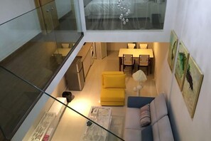 A compact living space with a glass balcony, a sofa, a yellow ottoman, a dining table with chairs, and a small kitchen area. - Lemon Heart Apartment Hotel (Foshan)