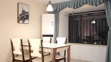Un coin repas avec une table et des chaises, un luminaire suspendu, une fenêtre avec des barreaux et un climatiseur fixé au mur.