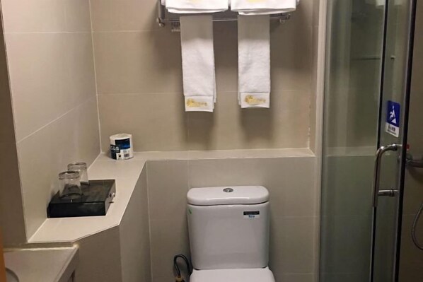A bathroom with a toilet, a glass shower enclosure, and a small shelf with a bottle and a glass. - Lemon Heart Apartment Hotel (Foshan)