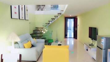 A modern living room with a sofa, a yellow chair, a television, and a staircase leading to an upper level.