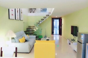 A modern living room with a sofa, a yellow chair, a television, and a staircase leading to an upper level. - Lemon Heart Apartment Hotel (Foshan)