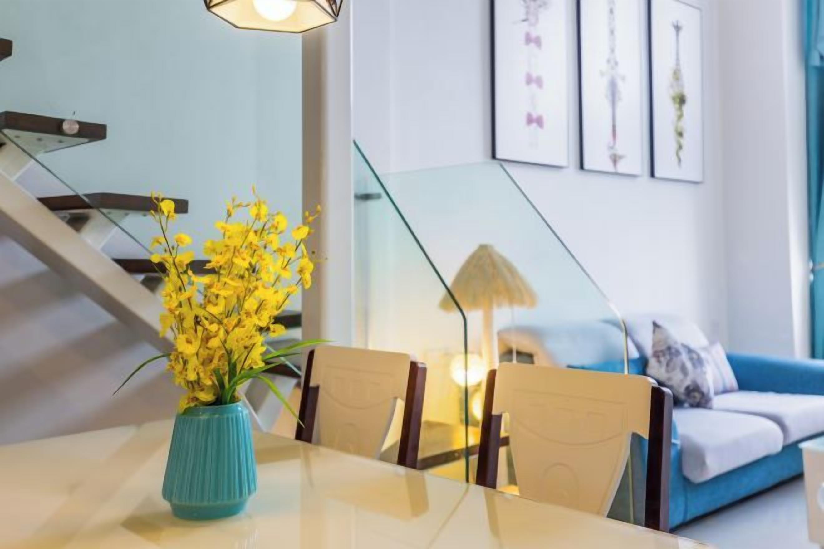 A dining area with a table, chairs, a vase of yellow flowers, and a staircase in the background.