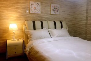 A neatly made bed with white linens and striped pillows, a bedside lamp, and two framed artworks on the wall. - Lemon Heart Apartment Hotel (Foshan)