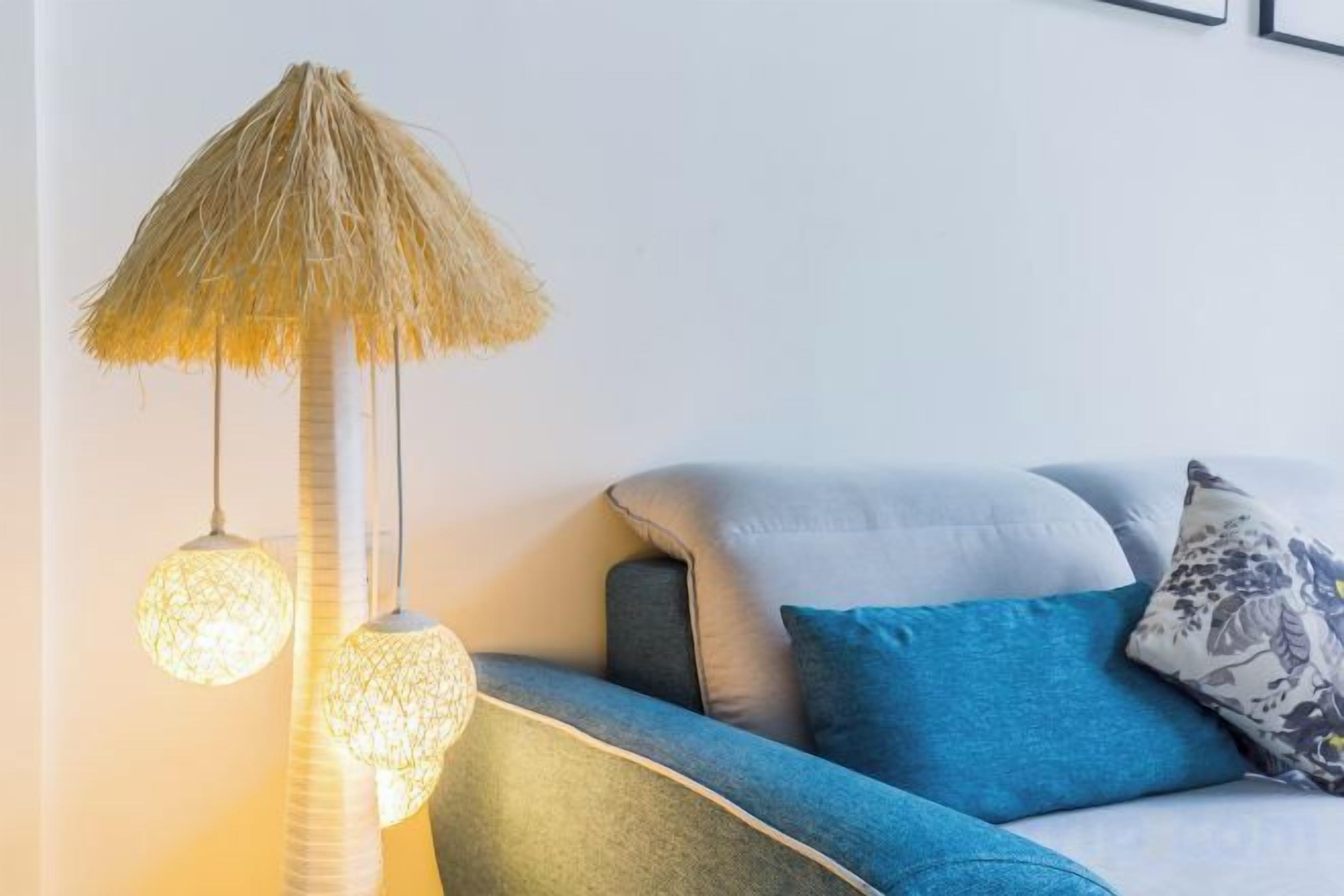 Une pièce avec un canapé, une lampe dotée d’un abat-jour en fibres naturelles et un coussin à motifs.