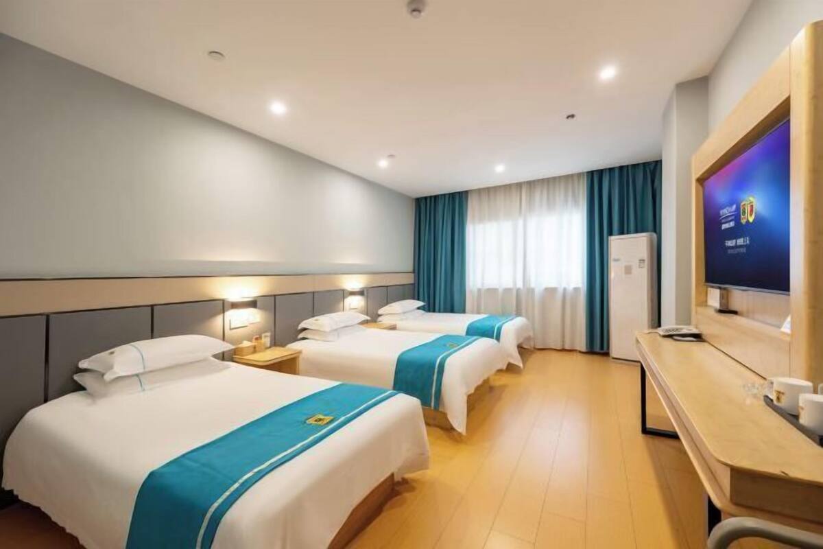 A hotel room with three beds, a TV, a desk, and a window with curtains.