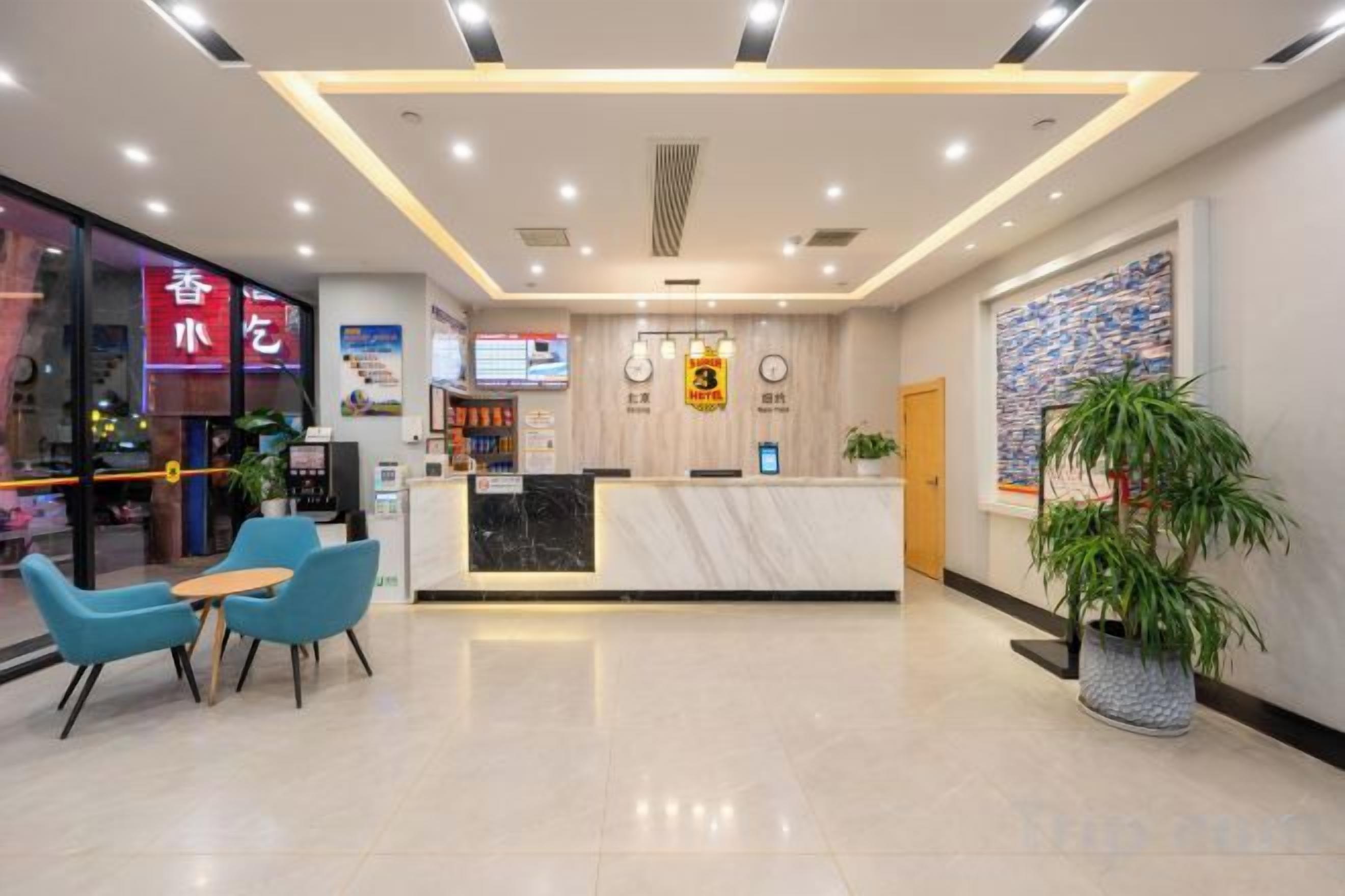 A hotel reception area with a marble counter, blue chairs, a potted plant, and a large artwork on the wall.