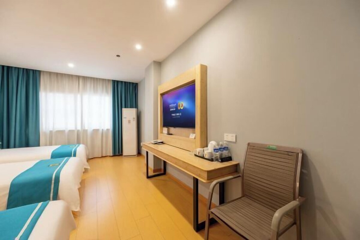 A hotel room with two beds, a desk, a chair, a TV, and a window with curtains.
