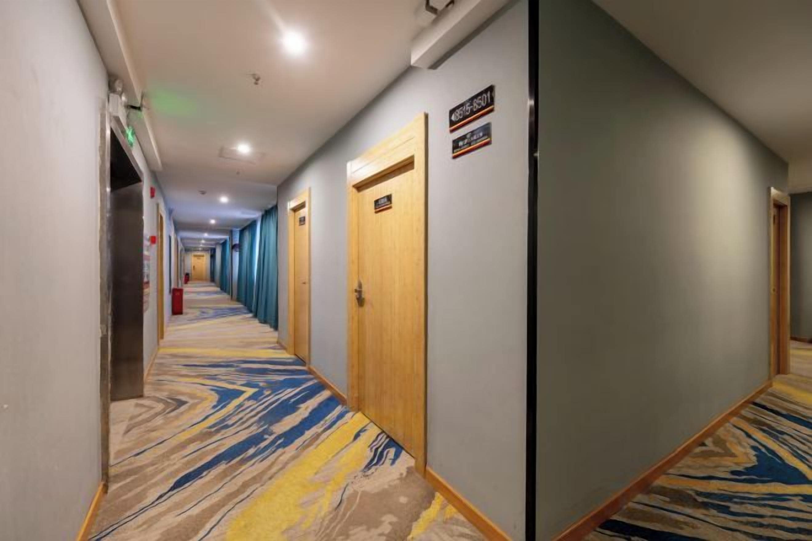 Een hotelgang met deuren aan beide kanten, een kamergestreept tapijt en een bordje dat de beschikbaarheid van kamers aangeeft.