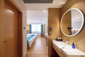 A hotel room with a wooden door, a large round mirror, a white sink, and a bed with blue bedding.