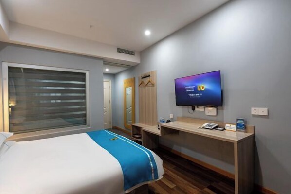 Une chambre d’hôtel comprenant un lit, un bureau avec un téléviseur à écran plat, une fenêtre avec des stores et un miroir.