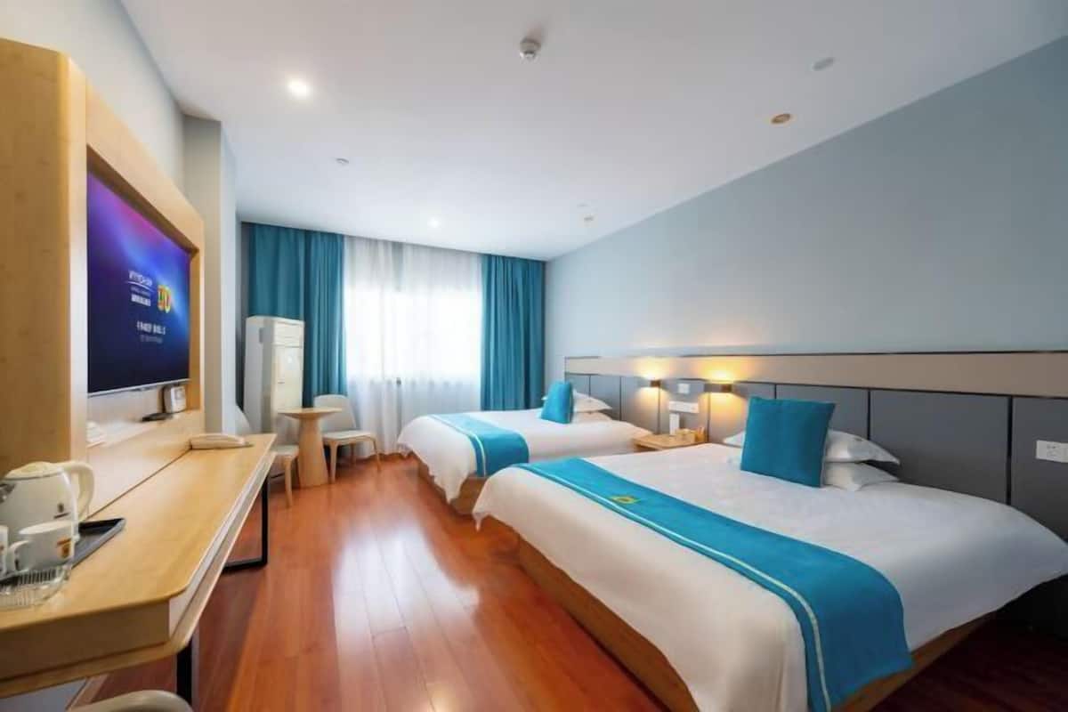 A hotel room with two beds, a desk with a computer, a TV, and a window with curtains.
