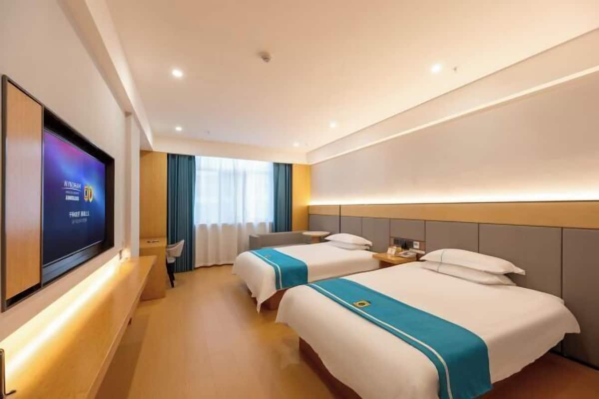 A hotel room with two beds, a TV, a desk, and a window with curtains.