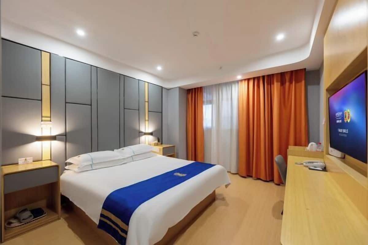 A hotel room with a bed, bedside tables, a desk, a TV, and curtains.