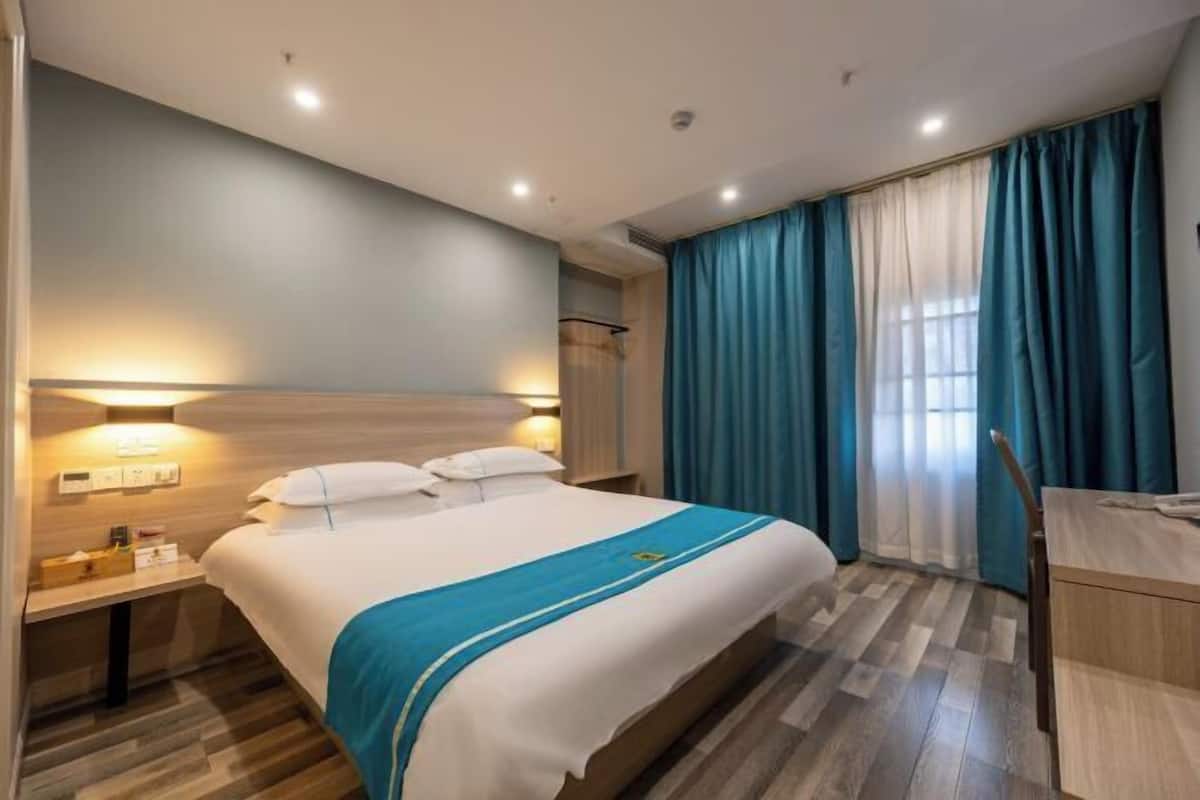A hotel room with a bed, bedside table, lamp, curtains, and a desk.