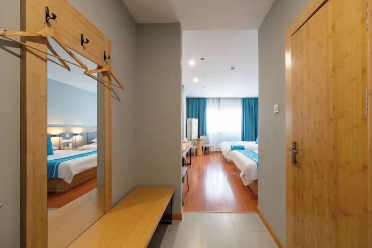 A hotel room with a wooden bench, a mirror, and a bed with a blue bedspread.