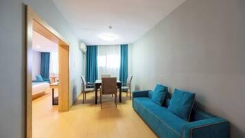 Ein modernes Hotelzimmer mit einem blauen Sofa, einem Esstisch mit Stühlen und einem separaten Schlafbereich mit einem Bett.