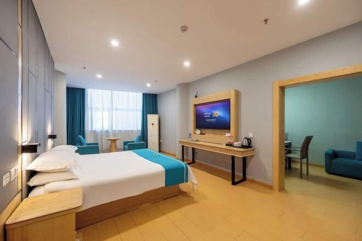 A hotel room with a bed, a desk, a television, and a seating area.