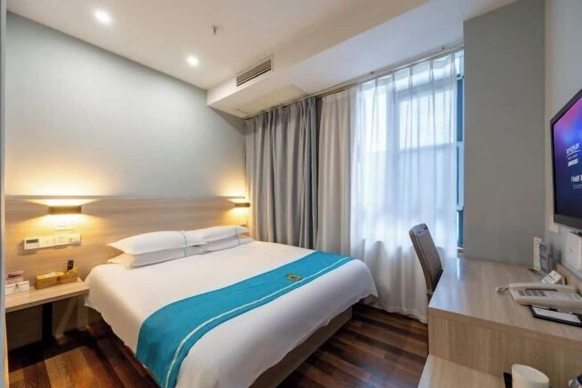 A hotel room with a bed, desk, chair, TV, and curtains.