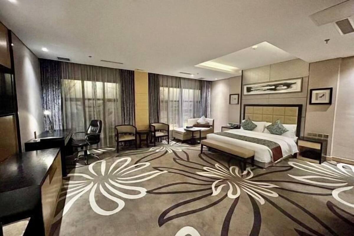 Una habitación de hotel con cama, escritorio, silla, sofá y una ventana grande con cortinas.