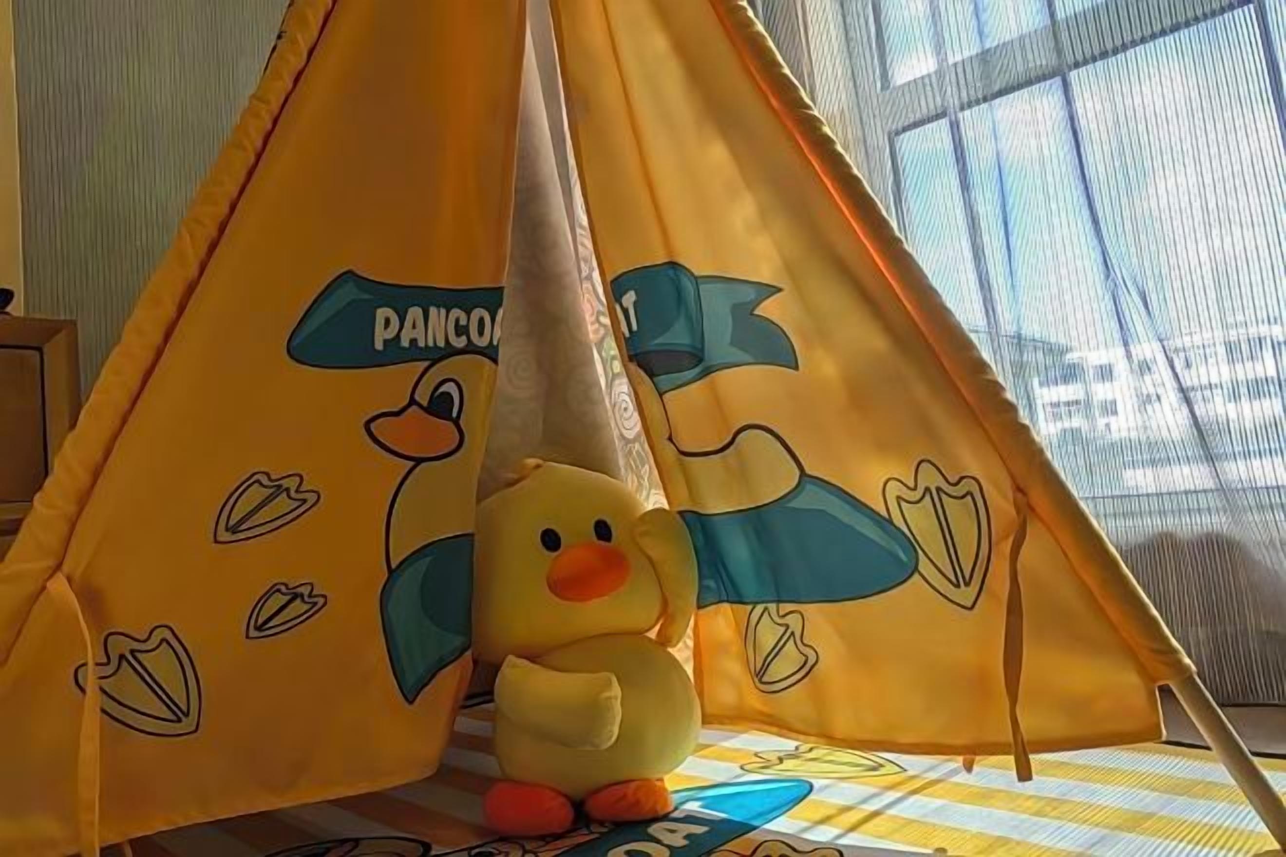A yellow tent with duck designs and a plush duck toy inside.