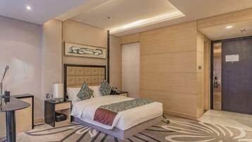 Una habitación de hotel moderna con una cama grande, una mesita de noche, un cuadro en la pared y una puerta de madera.