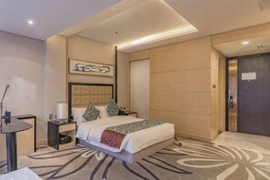 A modern hotel room with a large bed, a bedside table, a nightstand, a wall-mounted artwork, and a wooden door. - Ziyu International Holiday Hotel (Chengde)