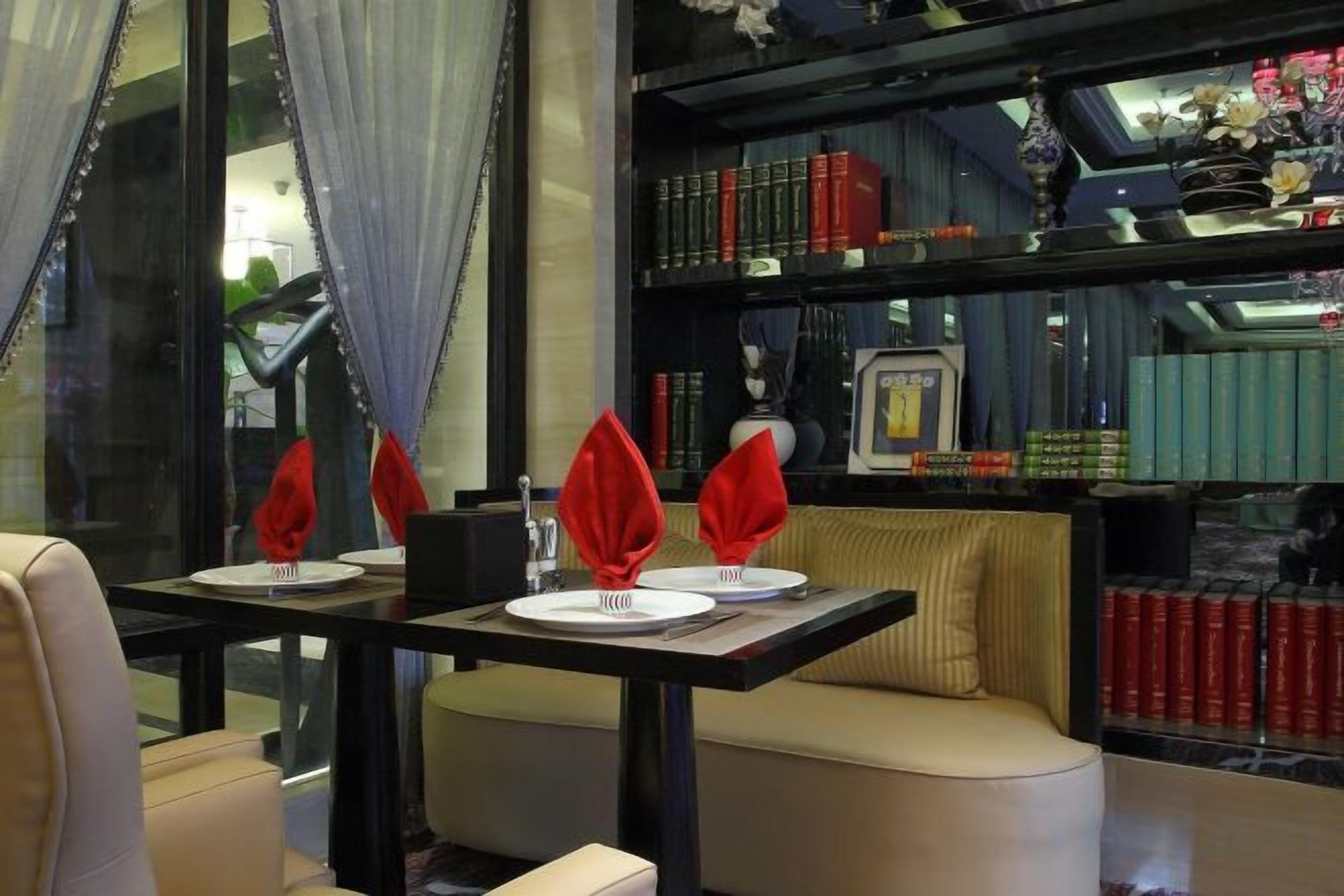 Un comedor con una mesa dispuesta para dos, una estantería al fondo y una ventana con cortinas.