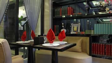 Un comedor con una mesa dispuesta para dos, una estantería al fondo y una ventana con cortinas.
