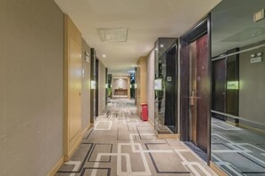 Un pasillo de hotel con alfombra estampada, puertas y un bote de basura.