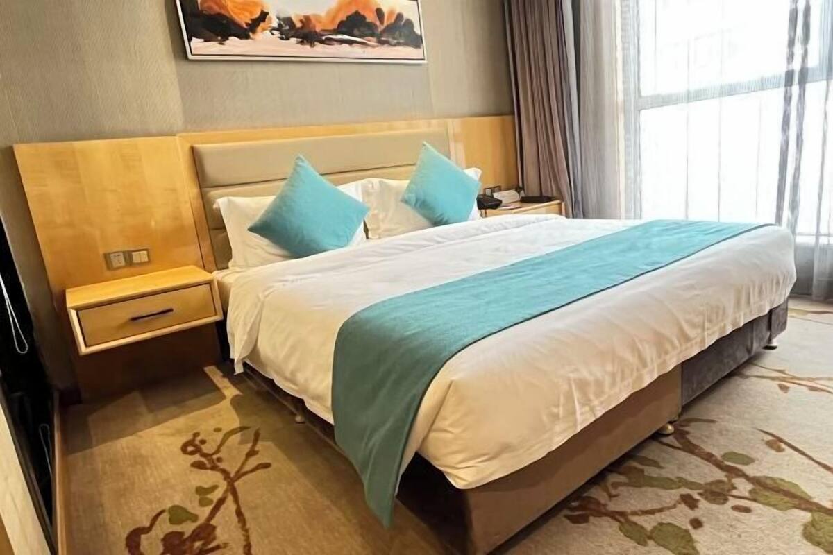 Habitación de hotel con una cama grande, una mesita de noche, un teléfono en la pared y un ventanal con cortinas.