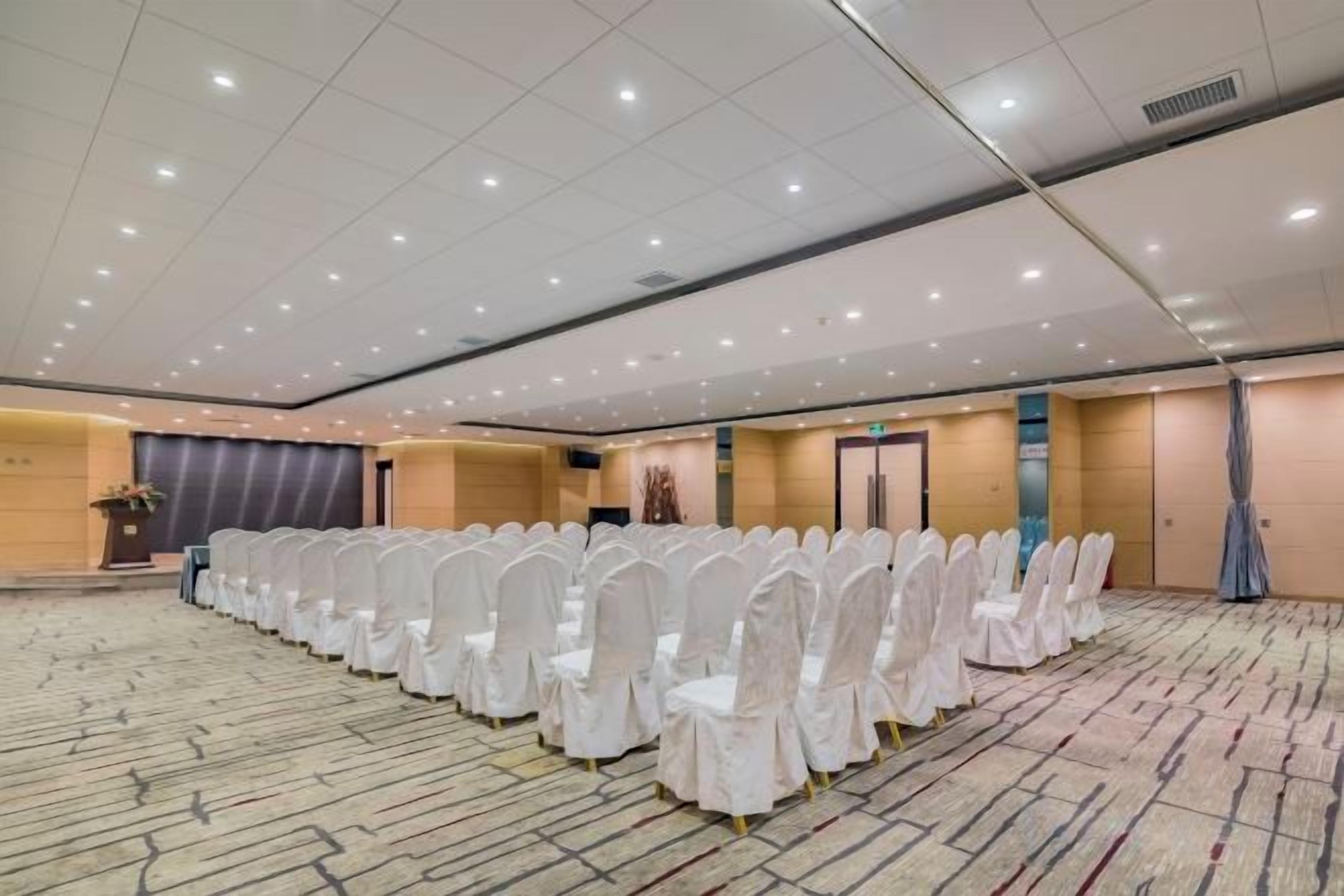 A large conference room with rows of white chairs, a podium, and a carpeted floor.
