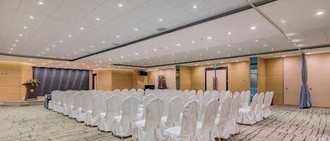 A large conference room with rows of white chairs, a podium, and a carpeted floor.