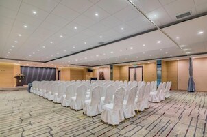 Un amplio salón de conferencias con filas de sillas blancas, un atril y suelo alfombrado.