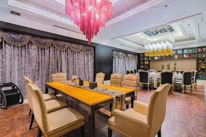 A dining area with a wooden table and chairs, a chandelier, and a bookshelf in the background. - Ziyu International Holiday Hotel (Chengde)