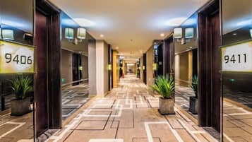 A hotel corridor with mirrored walls, numbered doors, and potted plants.
