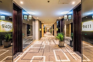 Corredor de hotel com paredes espelhadas, portas numeradas e vasos com plantas.