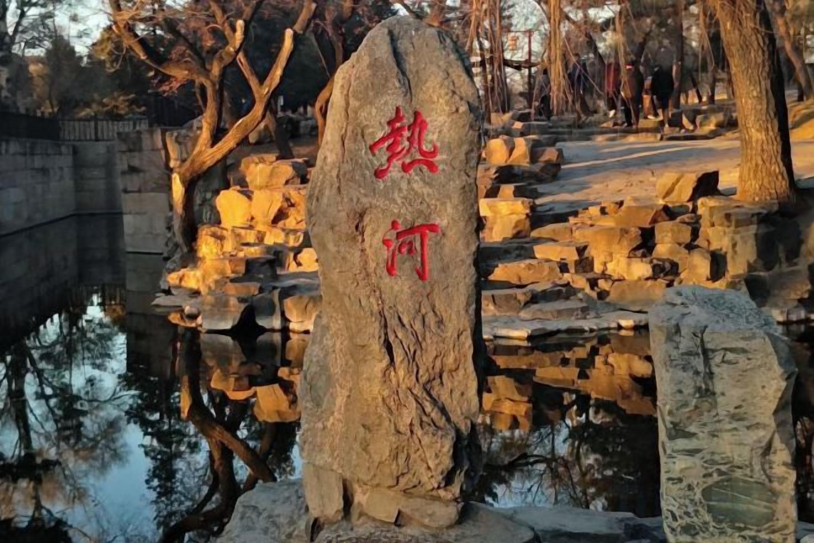 Um monumento de pedra com inscrições, rodeado por estruturas de pedra e um corpo de água.