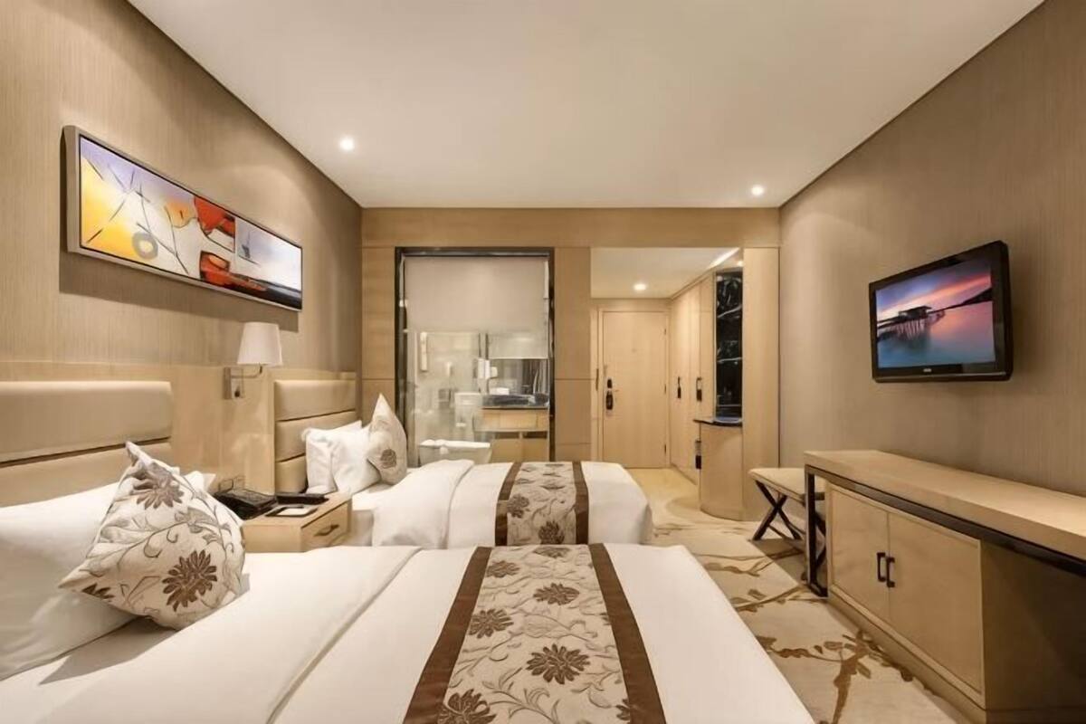 Habitación de hotel con dos camas, un escritorio, un televisor y un baño visible a través de una puerta abierta.