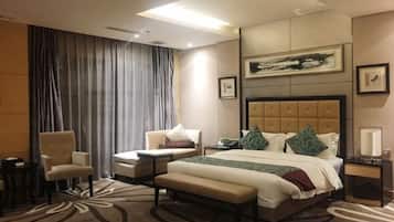 A hotel room with a large bed, two armchairs, a bench, a desk, and a large window with curtains.
