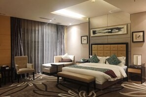 A hotel room with a large bed, two armchairs, a bench, a desk, and a large window with curtains. - Ziyu International Holiday Hotel (Chengde)