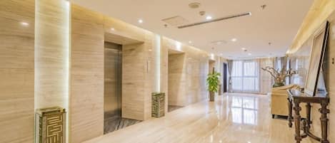 A hotel corridor with marble flooring, a reception desk, and a large window.