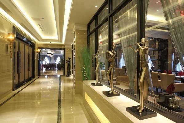 Un couloir dâhĂŽtel avec un sol cirĂ©, de grandes fenĂȘtres et des mannequins prĂ©sentant des vĂȘtements.