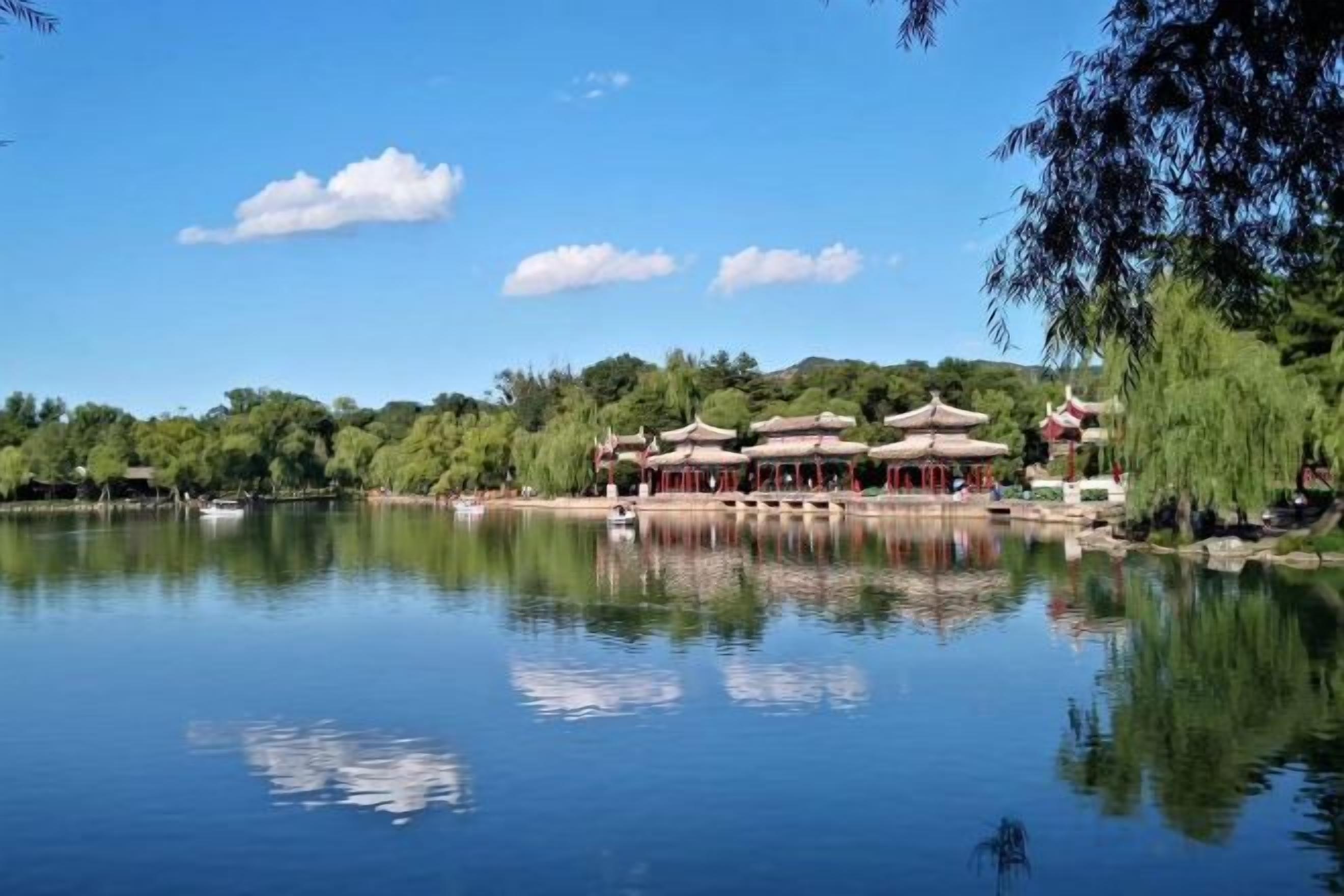 En rogivande miljö vid en sjö med traditionell arkitektur, inklusive en paviljong och en byggnad med ett välvt tak, omgiven av frodig grönska.