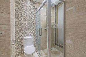 Kylpyhuone, jossa on wc, lasiovilla varustettu suihku ja laatoitettu seinä.