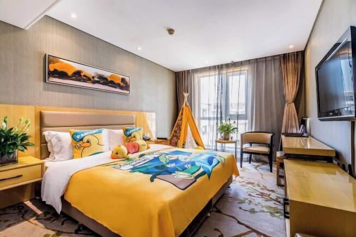 Una habitación de hotel con cama, escritorio, silla, televisión y ventana con cortinas.