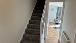 Eine Treppe mit Teppichstufen führt zu einem Raum, der einen weißen Heizkörper, ein graues Sofa und einen Teppich auf dem Boden beinhaltet.