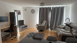 Ein modernes Wohnzimmer mit Flachbildfernseher, Schreibtisch, bequemer Couch und Esstisch.