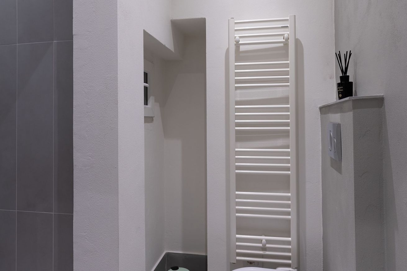 A bathroom with a white tiled wall, a white towel rack, and a black bottle of reed diffuser on a shelf.
